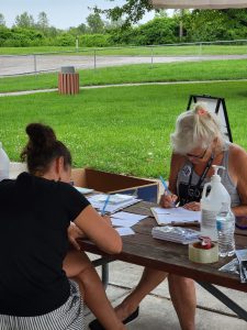 photos of picnic. handmade signs. women writing postcards outdoors. smiling faces.